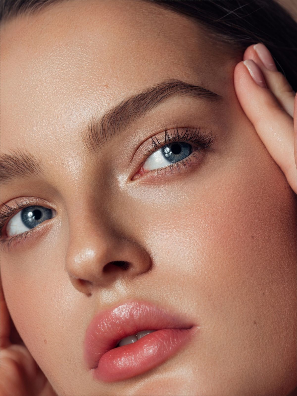a close shot of a woman with blue eyes and smooth skin. one of her hand is pulling against the skin along her temple